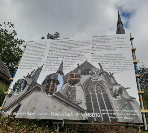 Het bord trekt onze aandacht niet alleen naar de tekst maar ook naar de kerk iets hoger gelegen 