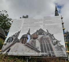 Het bord trekt onze aandacht niet alleen naar de tekst maar ook naar de kerk iets hoger gelegen 