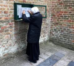Een zuster hangt een blad met richtlijnen uit aan de Begijnhofkerk in Brugge. © Lieve Wouters