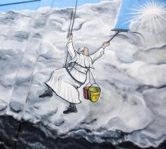 Graffitikunstenaar Mauro Pallotta maakte in 2019 in Albano (Italië) deze muurschildering: paus Franciscus hangt als een bergbeklimmer aan een touw en veegt de vervuilende rook van een fabriek weg. Op zijn emmertje staat ‘Laudato Si’.  © KNA