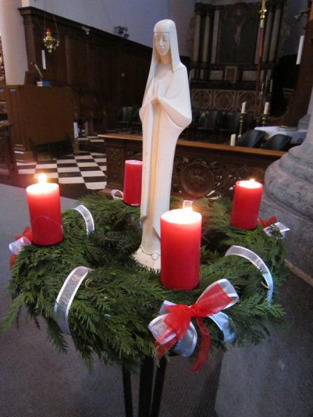 Adventskrans met O.L.-Vrouw in het midden die in ‘verwachting’ is, die haar kind verwacht. 