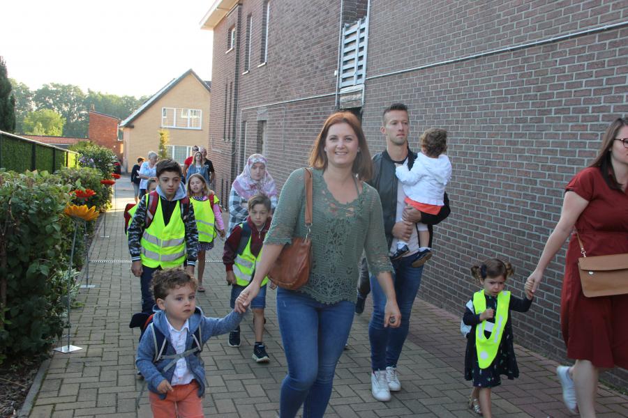 Ouders en grootouders begeleiden de kinderen naar school op de eerste schooldag waar ze vriendelijk onthaald worden tussen kleurrijke bloemen. 