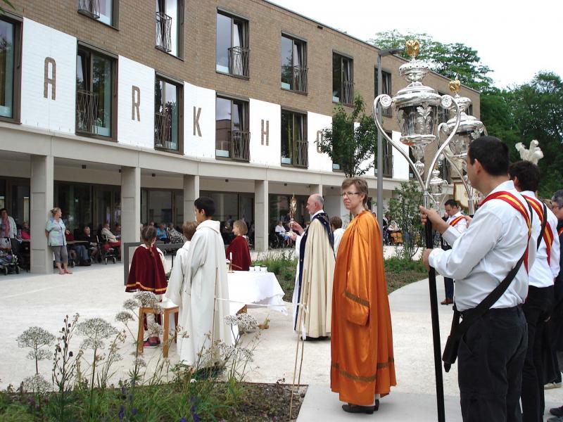 De bewoners van het Parkhof zaten goed geschermd onder de galerij. Na de zegen maakte deken Piet Capoen tijd om met het Heilig Sacrament tot bij hen te gaan. © Lydia Van Buggenhout 