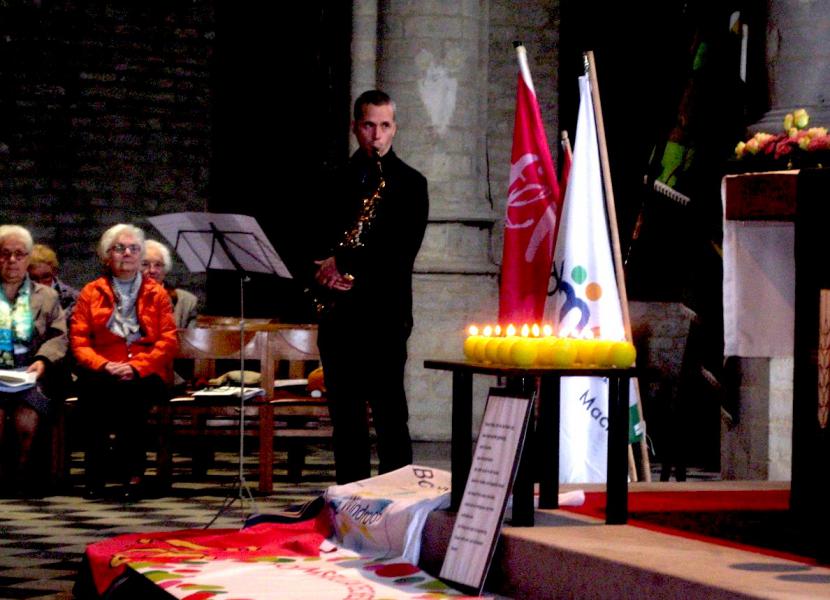 Cedric speelt saxofoon bij de brandende kaarsen: een voor elke beweging of werkgroep die mee wil bouwen aan het welzijn van onze parochiegemeenschap. © @L.J.