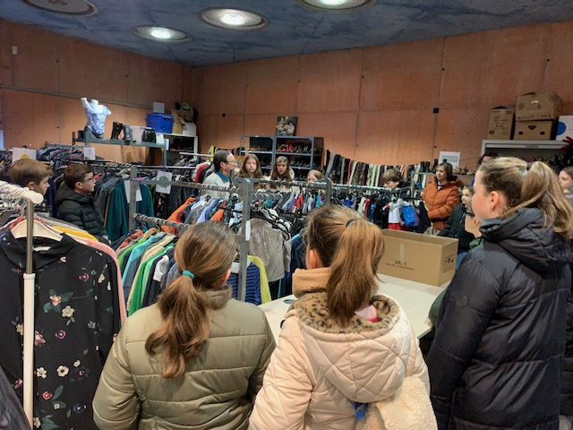François geeft uitleg tussen de rekken kleding. Naast voeding kan je er ook kledij kiezen. 