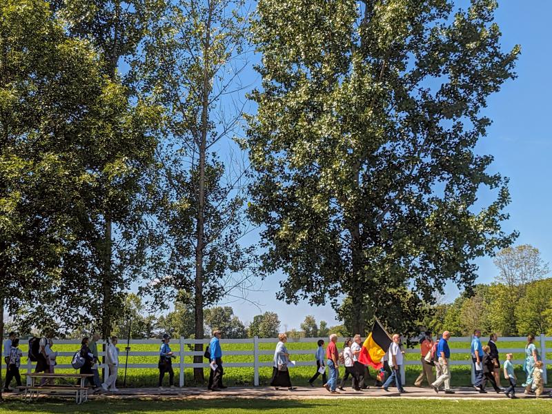 Gelovigen verzamelen zich in processie rond het terrein van het heiligdom, waarbij Henri Meulemans de Belgische vlag draagt © John Steffen