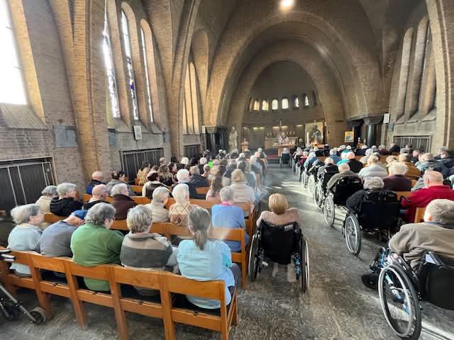 Een bomvolle Damiaankerk met heel veel rolstoelen en rollators 