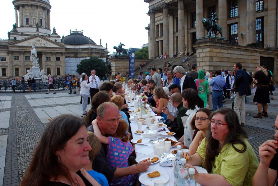 Deelnemers schuiven de voeten onder een lange tafel voor een vriendschapsmaal. 