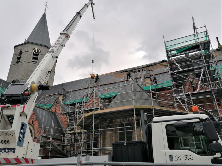Arbeiders op de daken trotseren weer en wind om lei na lei te monteren tot een waterdicht stevig dak. 