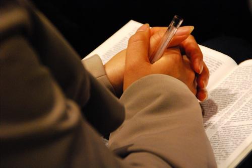 Een vrouw bidt met de Bijbel, pen in de hand. © Areta Ekarafi