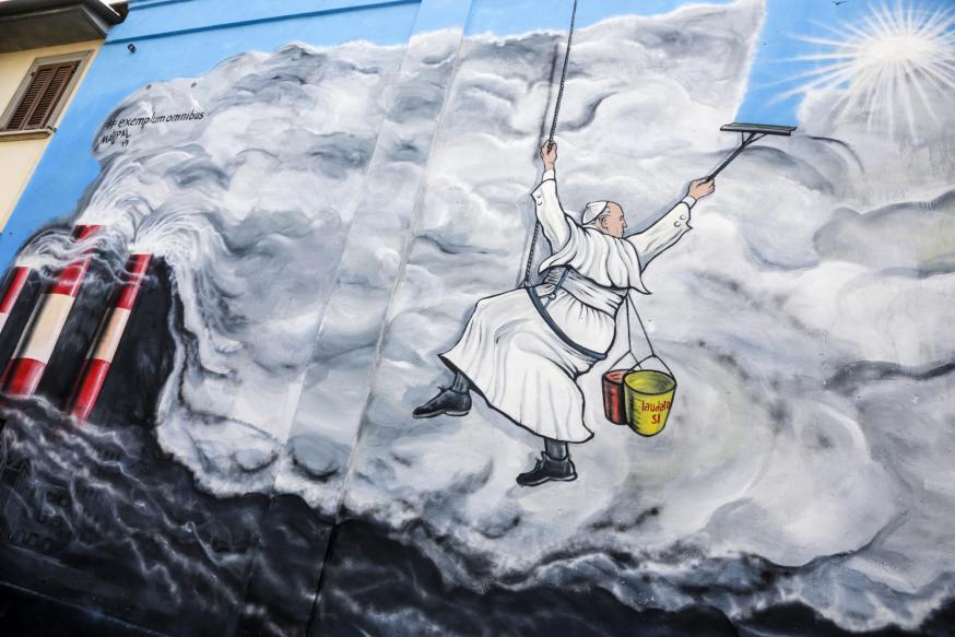 Graffitikunstenaar Mauro Pallotta maakte in 2019 in Albano (Italië) deze muurschildering: paus Franciscus hangt als een bergbeklimmer aan een touw en veegt de vervuilende rook van een fabriek weg. Op zijn emmertje staat ‘Laudato Si’.  © KNA