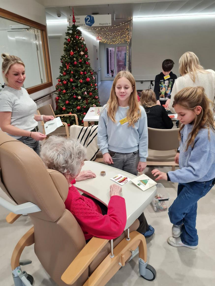 Twee kinderen uit De Klinge knutselen op het tabletje van de dame in de rolstoel 